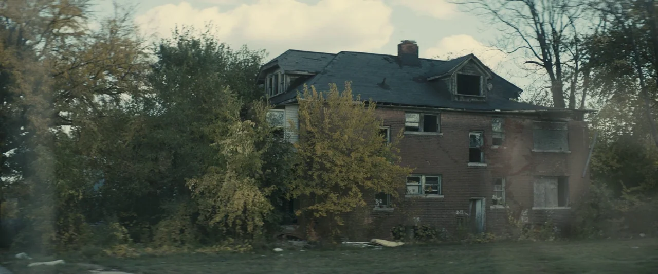 Don’t Breathe 2 (2021) movie still: establishing — A dilapidated, three-story brick house with broken windows sits nestled among overgrown autumn…