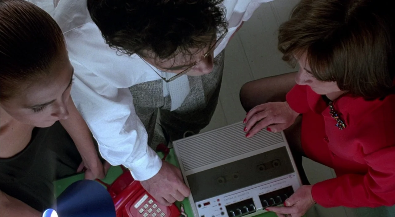 Women on the Verge of a Nervous Breakdown (1988) movie still: medium — An interior space with three people leaning over a desk. They are gathered…