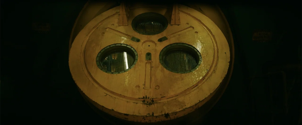 Meg 2: The Trench (2023) movie still: closeup — A yellow circular submarine escape hatch with three reinforced glass portholes dominates the view.…