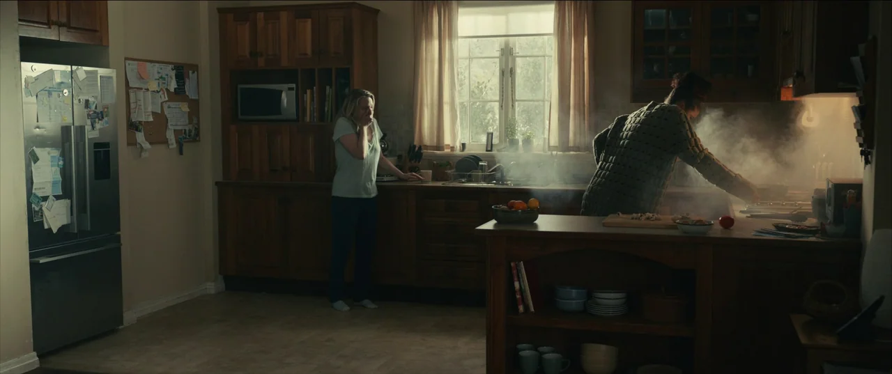 The Invisible Man (2020) (2020) movie still: wide — A residential kitchen features wooden cabinetry, a stainless steel refrigerator, and a central…
