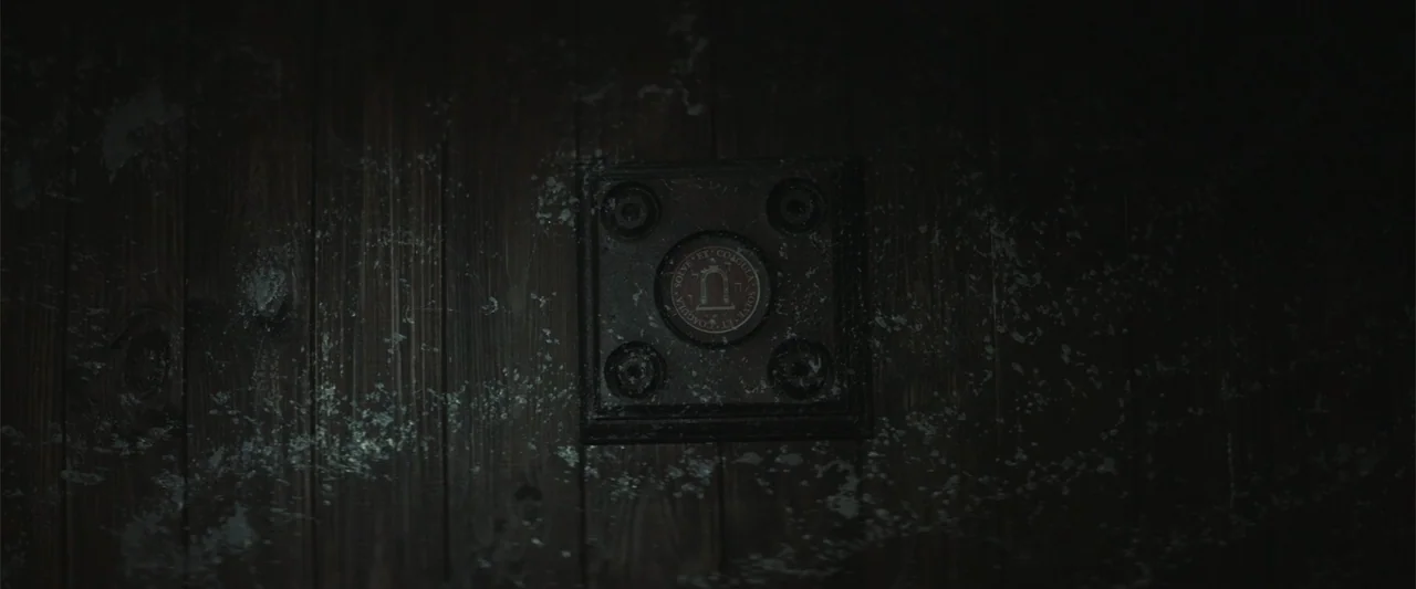 The Cellar (2022) movie still: closeup — A dark wooden door panel features a circular metallic insert with occult inscriptions. The surface of the…