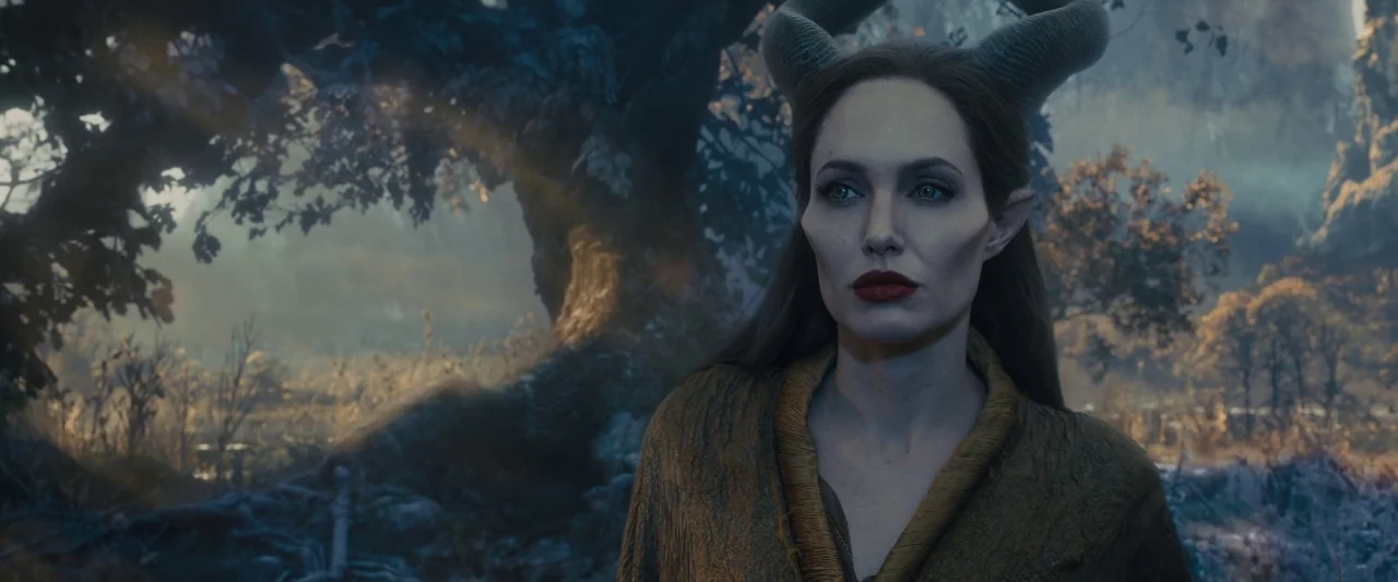 Maleficent (2014) movie still: medium — A dense, ancient woodland with thick twisted tree trunks and thick hazy atmospheric light. A horned woman…