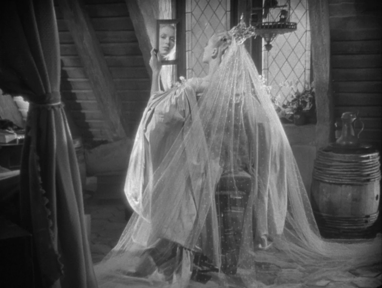 La Belle et la Bête (1946) movie still: medium — A wooden attic room contains a barrel, a birdcage, and a diamond-paned window. A woman wearing a…