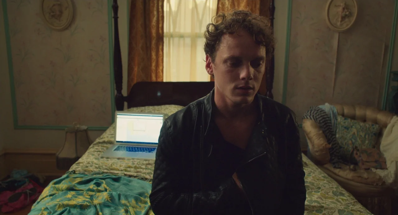 Cymbeline (2014) movie still: medium — A room with patterned floral wallpaper features a bed covered in a matching quilt. A man in a black leather…