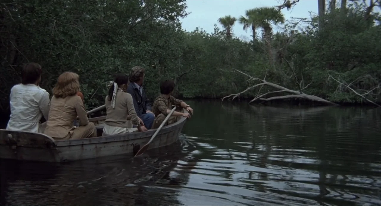 Empire of the Ants (1977) movie still: medium — A wooden rowboat carries five people through a narrow waterway lined with dense foliage. The group…
