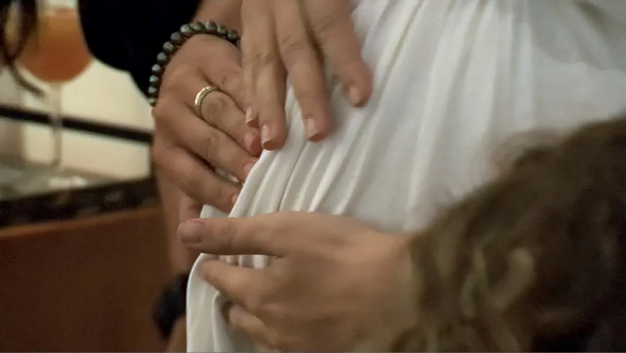 The (Dead Mothers) Club (2014) movie still: closeup — An interior space features two people placing their hands on a pregnant belly. The hands are…