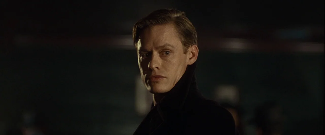 Kill Your Darlings (2013) movie still: closeup — A dimly lit room with dark walls provides the backdrop for a close-up shot. A man in a…