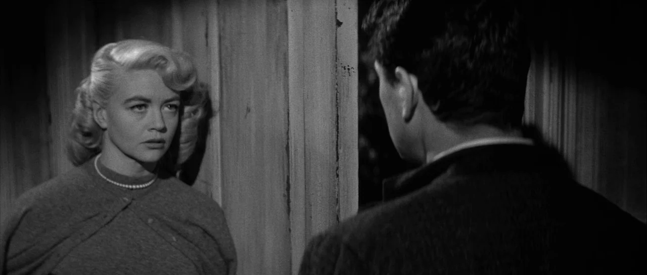 The Tarnished Angels (1957) movie still: medium — A dimly lit wooden doorway frames two individuals in a domestic interior setting. A blonde woman…