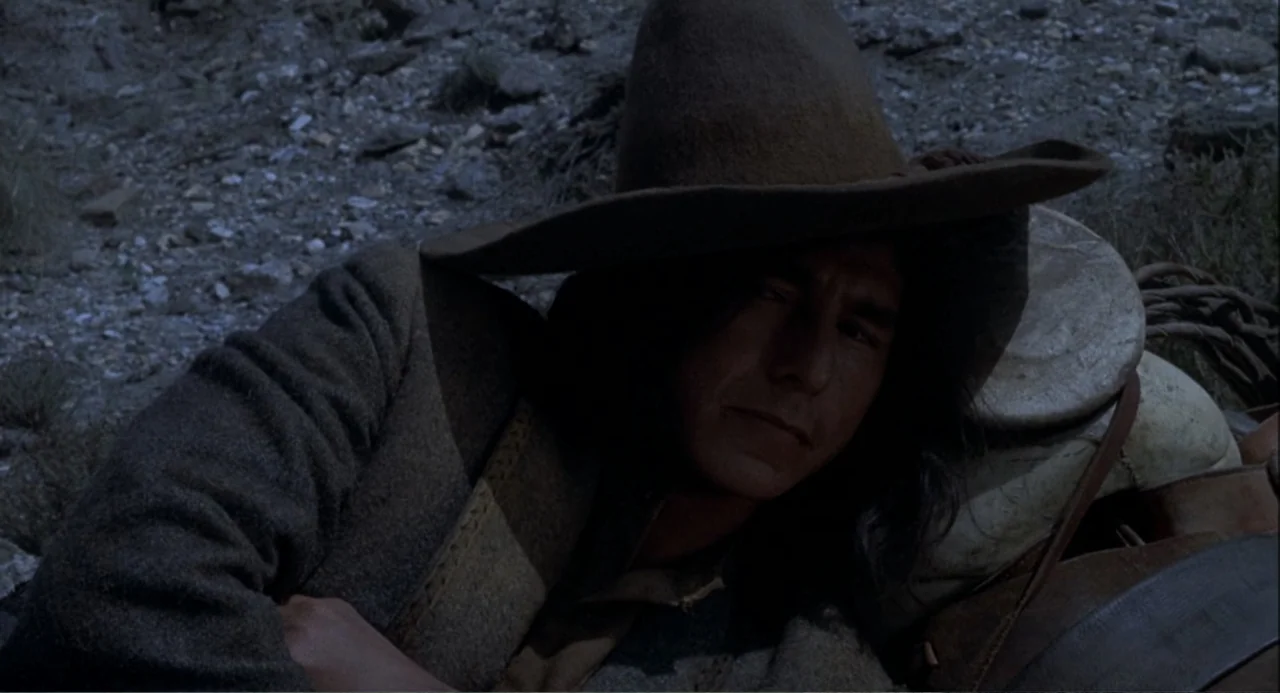 Chato's Land (1972) movie still: closeup — A dark, rocky patch of ground at night with sparse vegetation. A young man lies on the ground, leaning…
