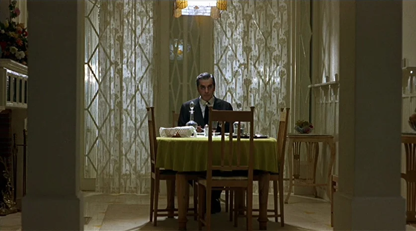 Juliet of the Spirits (1965) movie still: wide — A formal dining room features patterned curtains, a table with a green cloth, and wooden chairs. A…