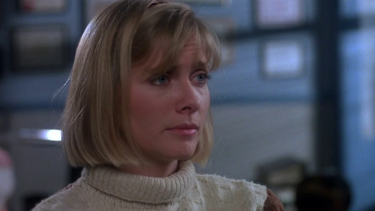 Re-Animator (1985) movie still: closeup — An interior space with blue walls adorned with framed certificates or papers in the back. A blonde woman…