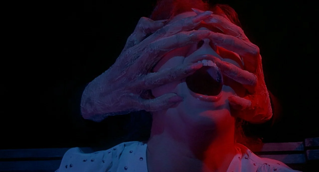 Inferno (1980) movie still: closeup — A person has their face obscured by two large, inhumanly textured hands. The person's mouth is wide open in an…