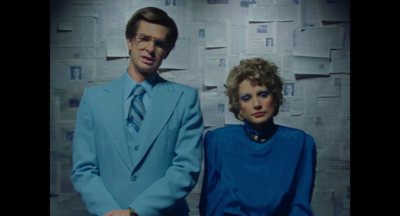The Eyes of Tammy Faye (2021) movie still: medium — Two individuals stand in front of a wall covered entirely in aged newspapers. The man wears a…