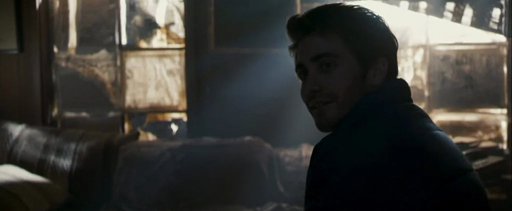Zodiac (2007) movie still: medium — A dark, dilapidated room contains a window covered in torn, grimy paper or film. A man in a dark jacket turns to…