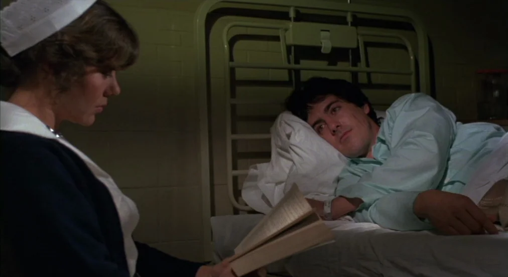 An American Werewolf in London (1981) movie still: medium — A dimly lit room contains a white hospital bed against a tiled wall. A nurse sits in the…