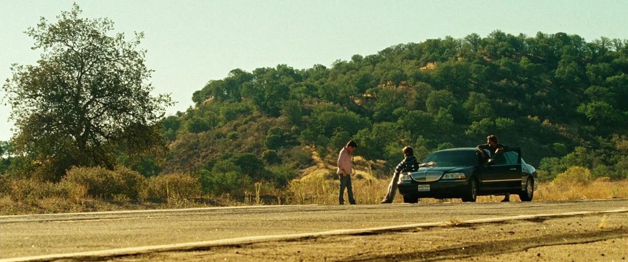 The Hangover Part III (2013) movie still: wide — A paved road runs through a dry, hilly landscape covered in low green brush. Three men gather near…