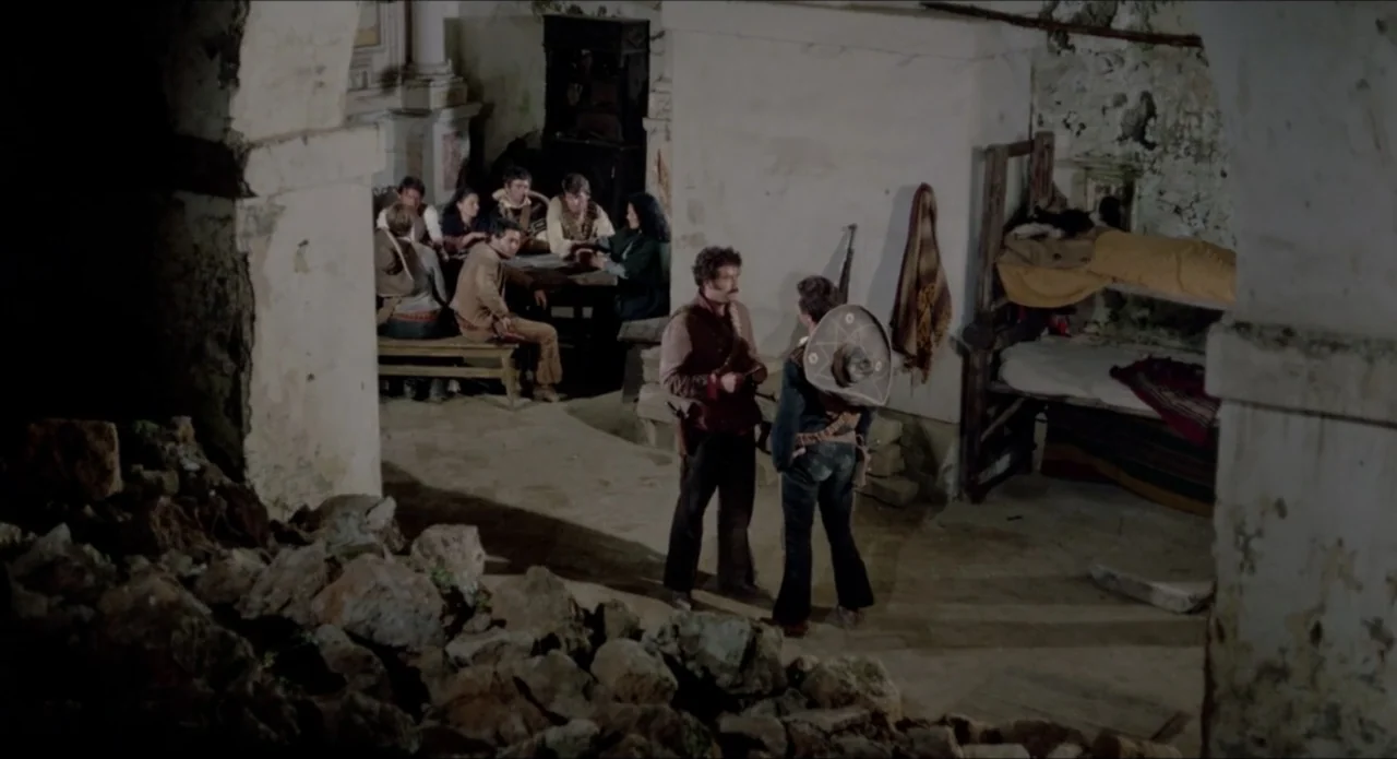 A Stranger in Town (1943) movie still: wide — A stone interior space with crumbling walls contains a group sitting at a table. Two men stand in the…