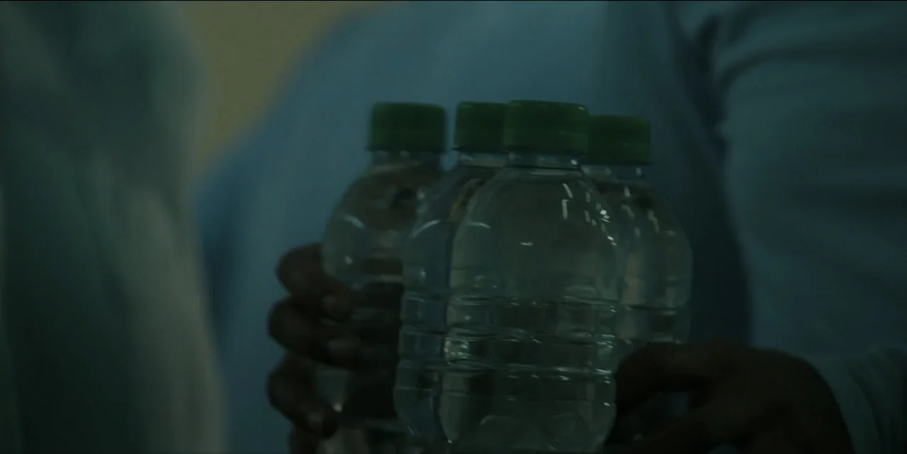 The Hunted (2024) movie still: closeup — A dimly lit indoor space features unidentified figures holding clear plastic water bottles. The focus is on…