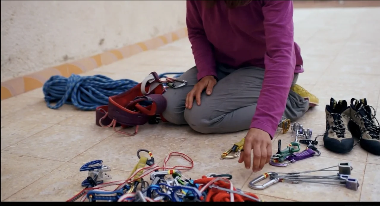 Crooked Trees Gon Give Me Wings (2022) movie still: medium — A person kneels on a paved outdoor terrace surrounded by various mountain climbing…