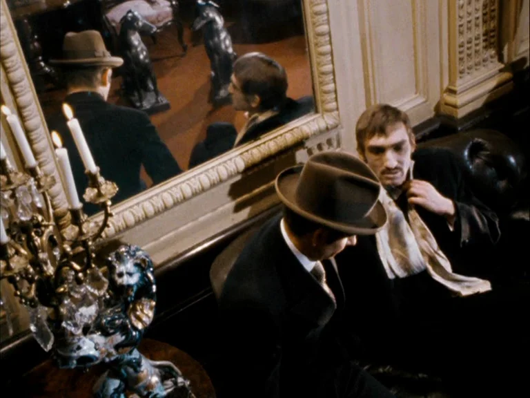 Making of: World On A Wire (1973) movie still: medium — A dimly lit room features a large mirror reflecting two men sitting together. A brass…