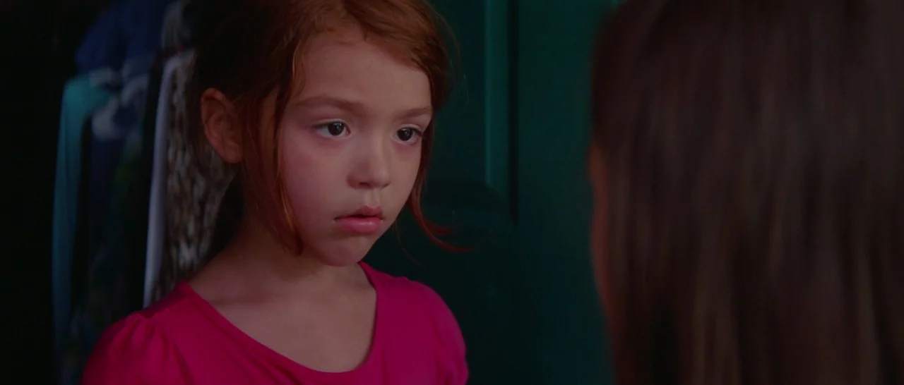 The Florida Project (2017) movie still: closeup — A dark closet interior contains hanging clothes visible in the background shadows. A young girl…