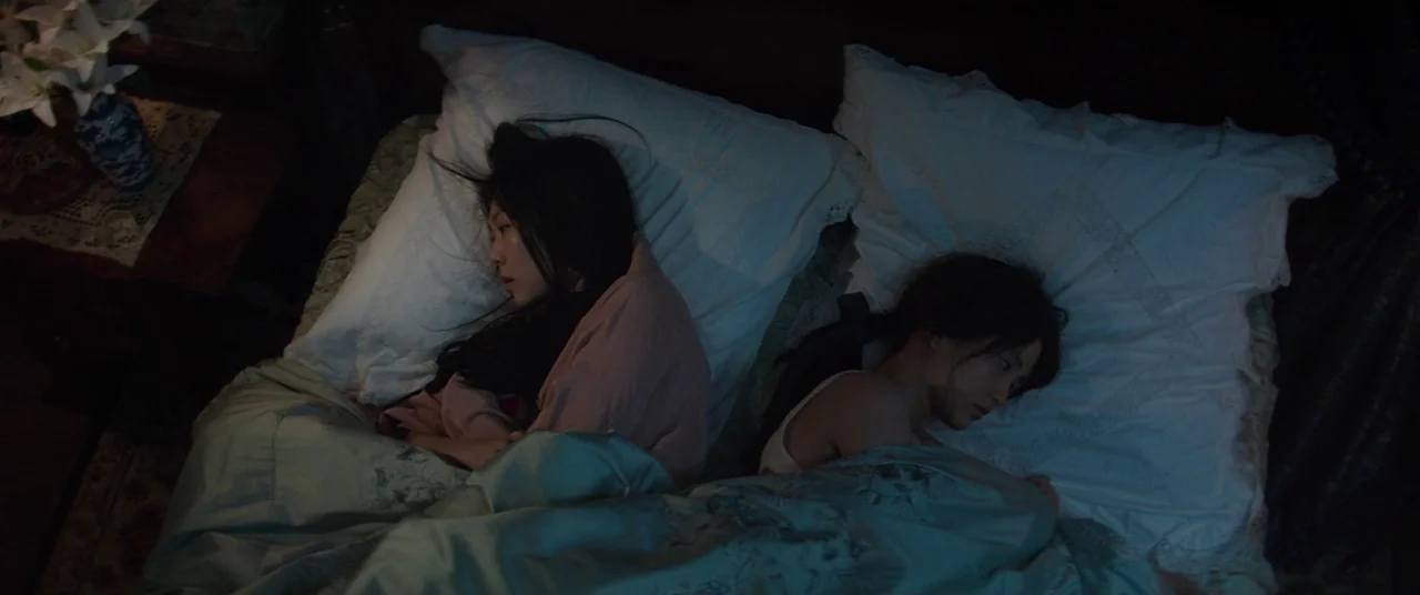 The Handmaiden (2016) movie still: medium — A dimly lit room features a mattress with white pillows and patterned teal covers. Two women lie…