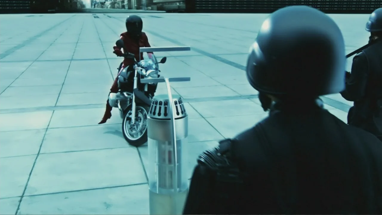 Ultraviolet (2006) movie still: wide — A vast, empty concrete plaza features a futuristic metal security device in the foreground. A woman on a…