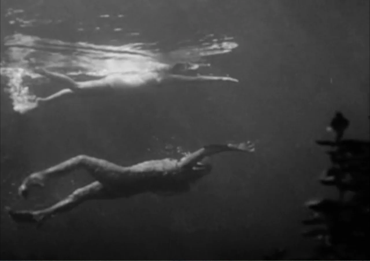 Creature from the Black Lagoon (1954) movie still: wide — Two figures move through the dark water in a deep aquatic environment. The pair swims…