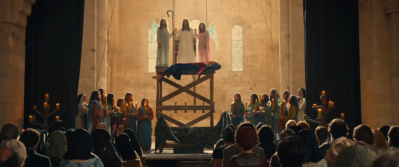 Benedetta (2021) movie still: wide — A stone cathedral nave features a central wooden scaffold holding three costumed figures elevated high. A large…