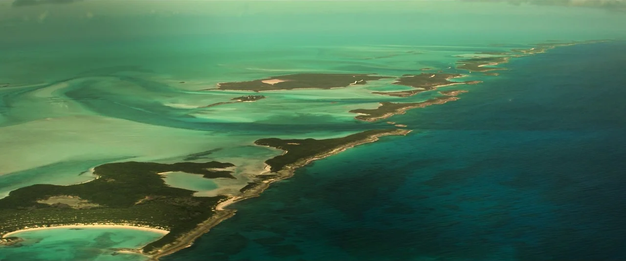 Black Widow (2021) movie still: establishing — An aerial view shows a chain of small, vegetated islands surrounded by shallow turquoise water. The…