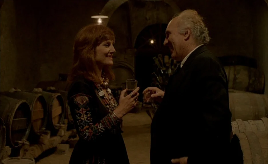 Milou en Mai (1990) movie still: medium — A dark, arched wine cellar contains rows of wooden barrels stored along the walls. A man in a suit and a…