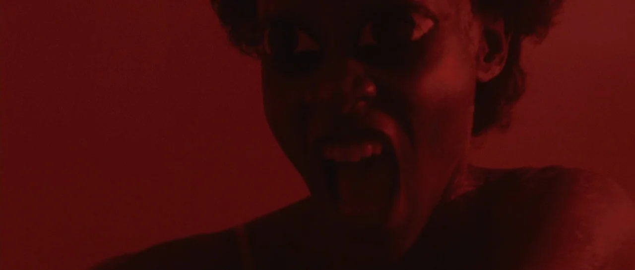 Message From The King (2016) movie still: closeup — A dark space is completely saturated in deep red light. A woman screams with her mouth wide open…