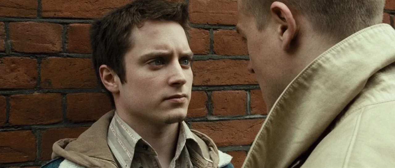 Green Street (2005) movie still: medium — An outdoor space featuring a red brick wall background behind two men. One man looks directly at the…