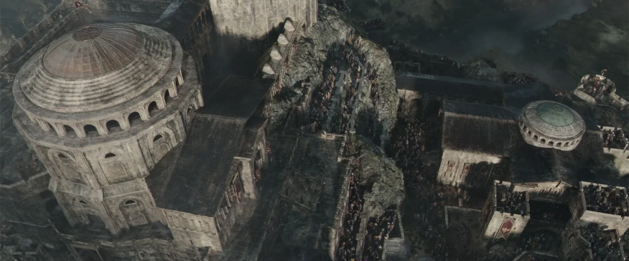 King Arthur: Legend of the Sword (2017) movie still: establishing — A vast stone fortress with domed roofs stands on a rocky hillside. Crowds of…
