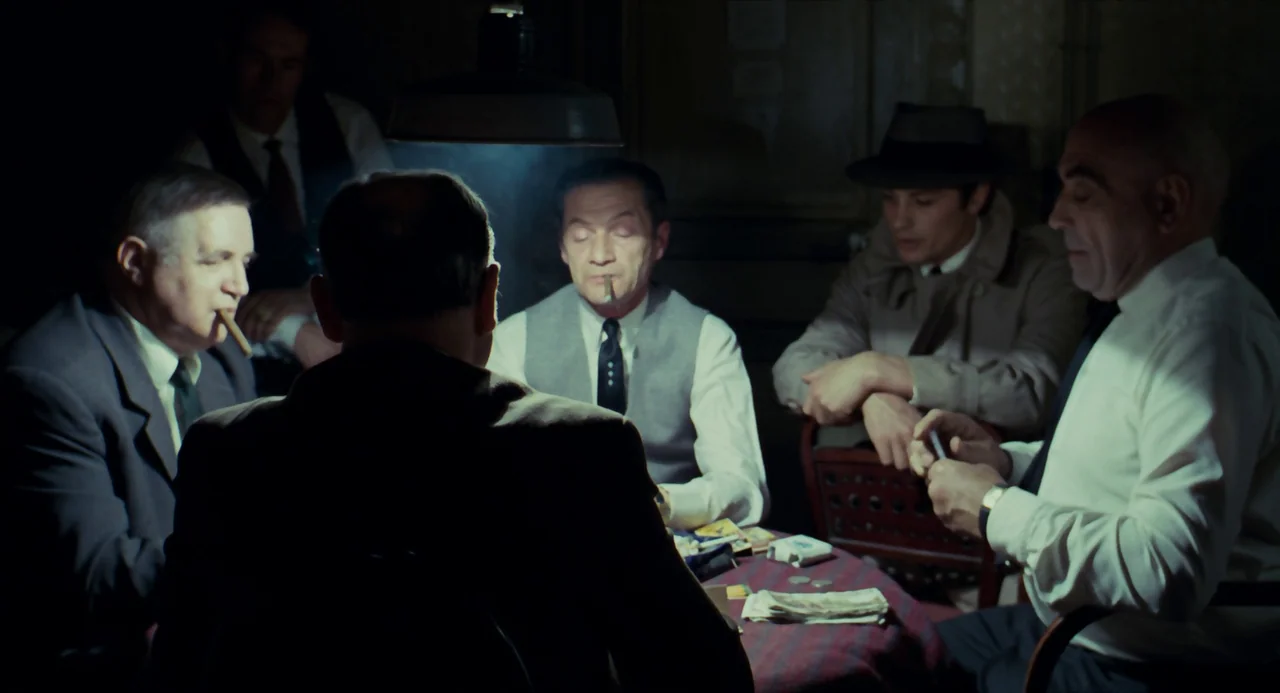 Le Samouraï (1967) movie still: medium — A dimly lit room features a group of men gathered around a circular table. They are playing cards while…