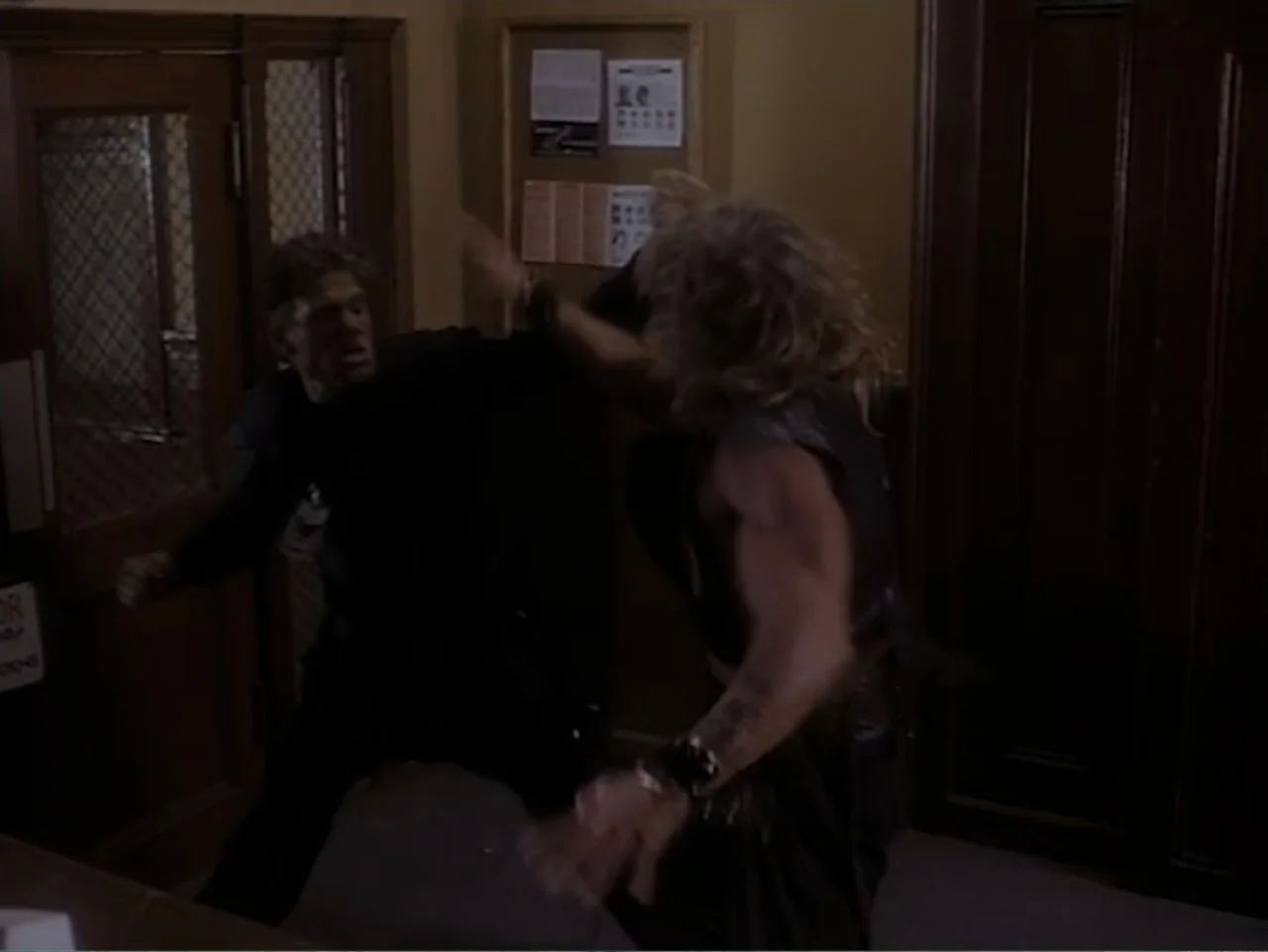 Firepower (1979) movie still: medium — An interior office hallway with a wooden door and a cork bulletin board. Two men are fighting in a…