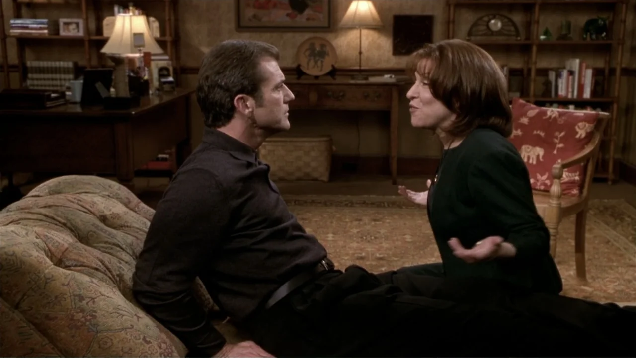 What Women Want (2000) movie still: medium — A study filled with wooden shelving, a desk, and a patterned rug. A man sits on a patterned couch while…