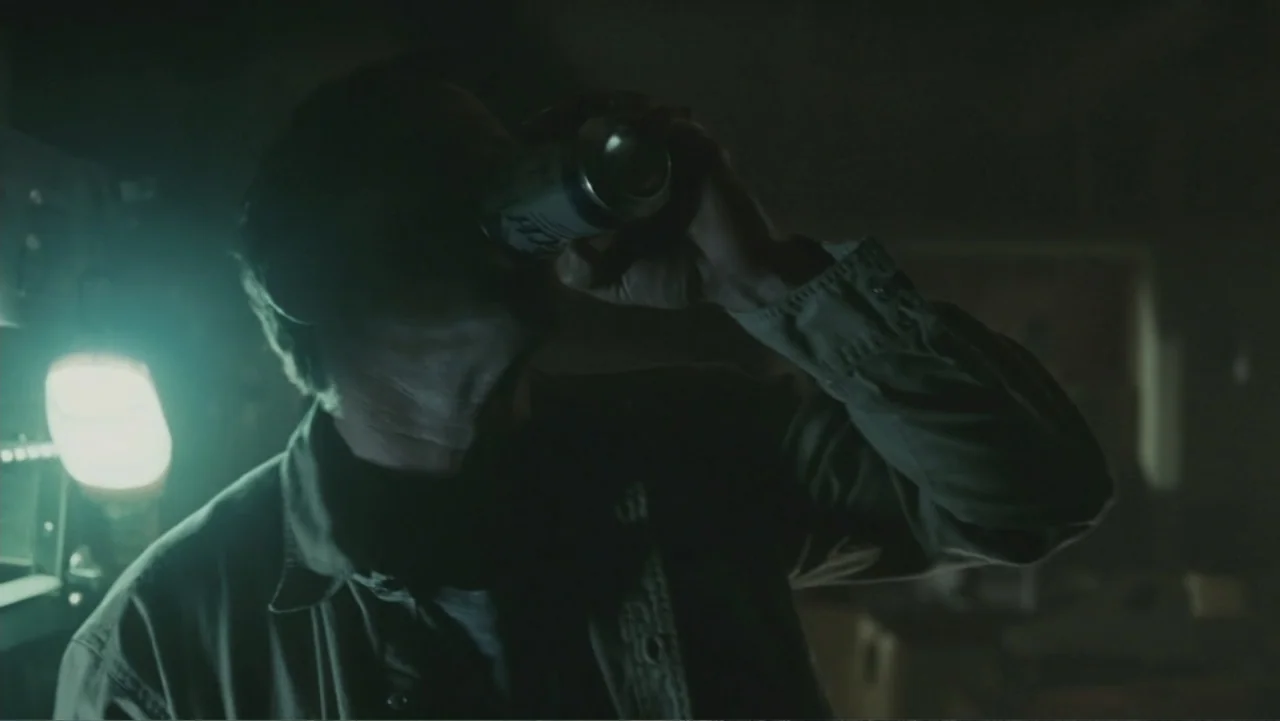 Legion (2010) movie still: medium — A dim workspace features a single glowing light fixture positioned against a dark wall. A man in a collared…