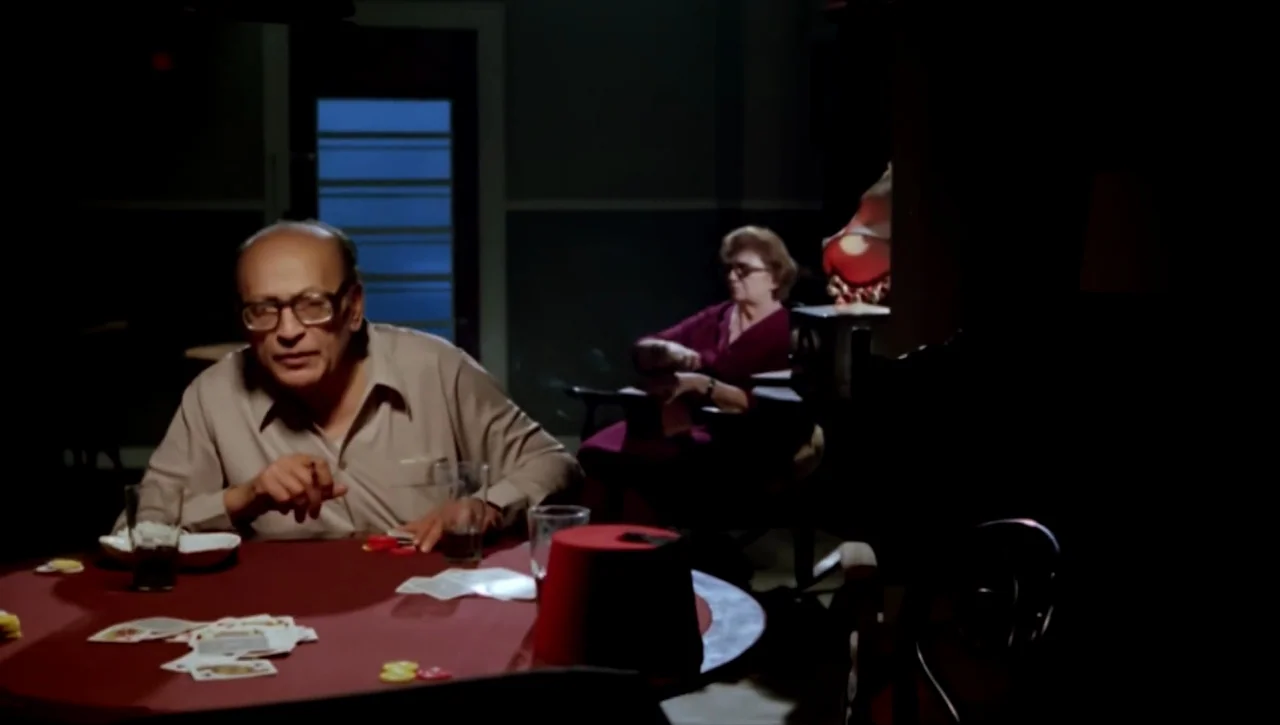 Alexandria…Why? (1979) movie still: medium — A dimly lit room with a circular table holding playing cards and poker chips. An elderly man plays…