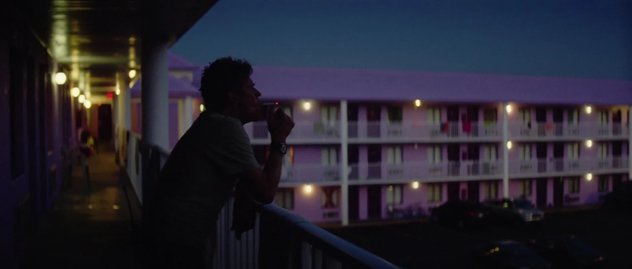 The Florida Project (2017) movie still: medium — A pink two-story motel building is illuminated against a dark evening sky. A man in silhouette…