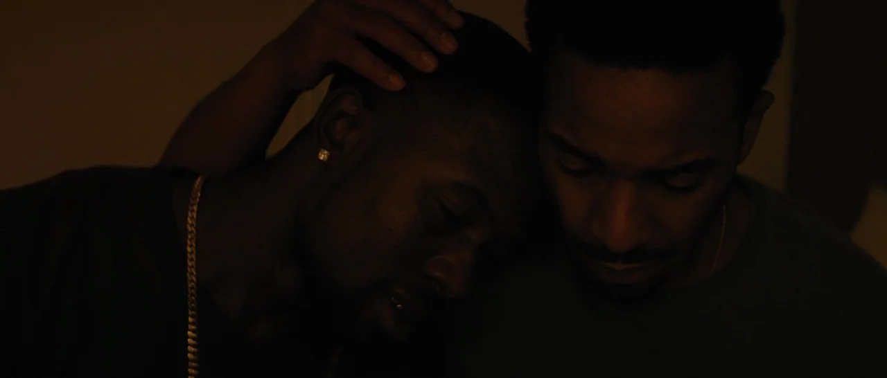 Moonlight (2016) movie still: closeup — A dark indoor space with minimal light sources surrounding two men. One man leans his head against the other…