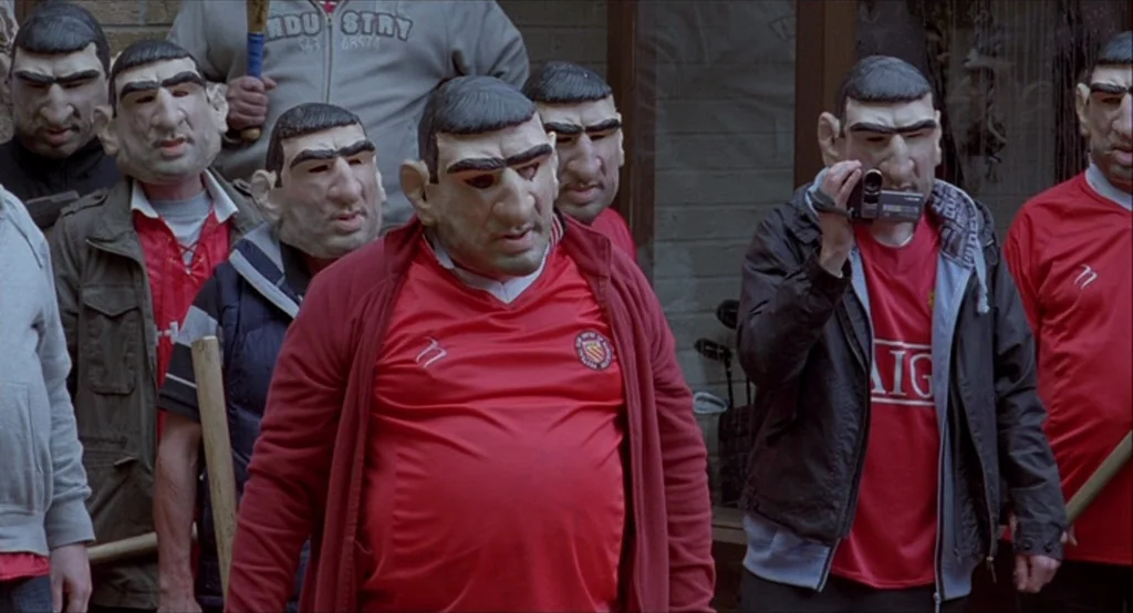 Looking for Eric (2009) movie still: medium — A group of men stand outside a building wearing identical, unflattering silicone face masks. One man…