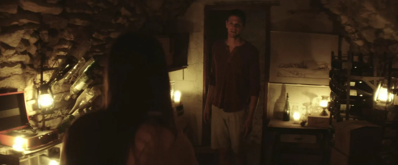 The Only One (2021) movie still: medium — A stone wine cellar with rustic walls and shelves filled with glass bottles. A man stands in the…