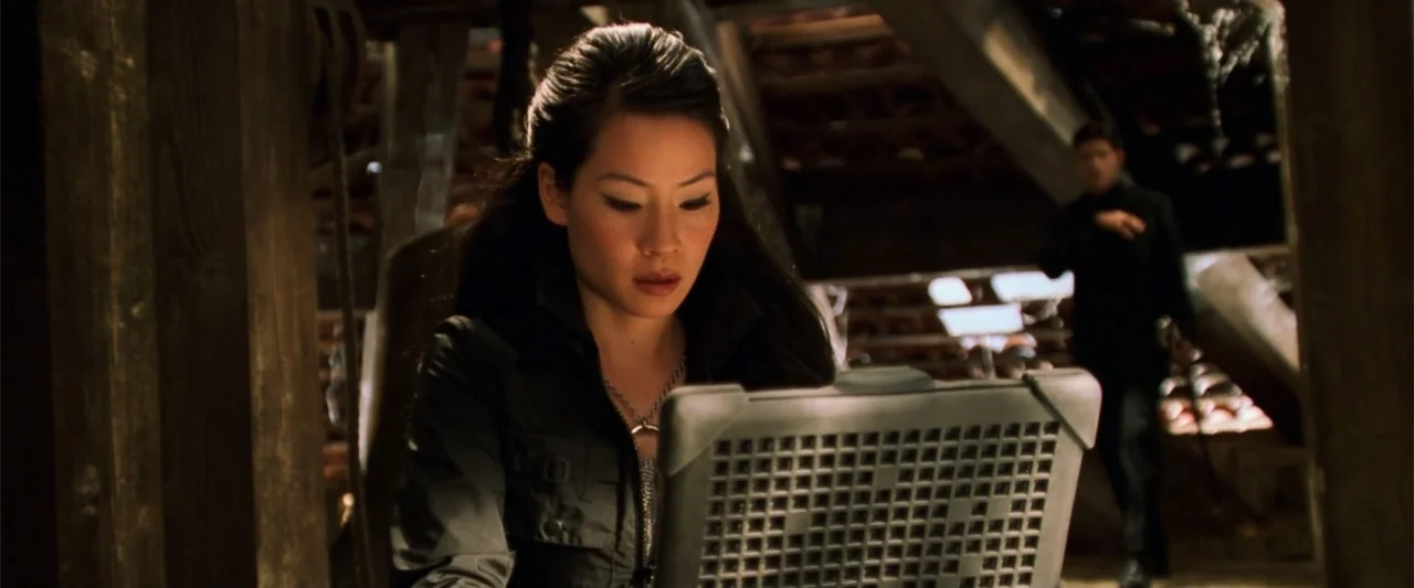 Charlie's Angels (2000) movie still: medium — A dark attic space with wooden support beams and dusty surroundings. A woman works on a laptop in the…