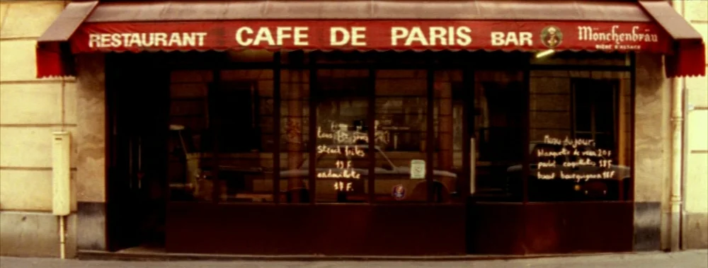 Carne (1991) movie still: establishing — The exterior facade of a restaurant and bar with a red canvas awning. Handwritten menu items are visible on…