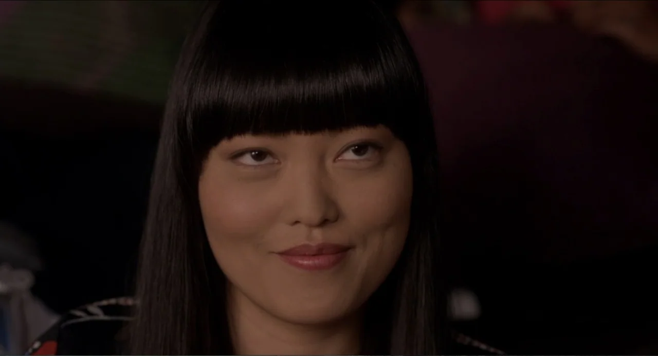 Pitch Perfect (2012) movie still: closeup — A close-up view of a young woman against a dark, featureless background. She faces the camera directly…