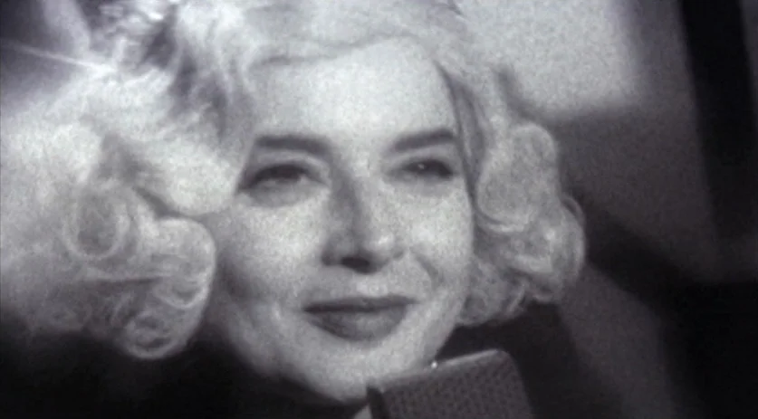 The Saddest Music in the World (2003) movie still: closeup — A close-up of a blonde woman in a radio studio with a microphone. The woman smiles…