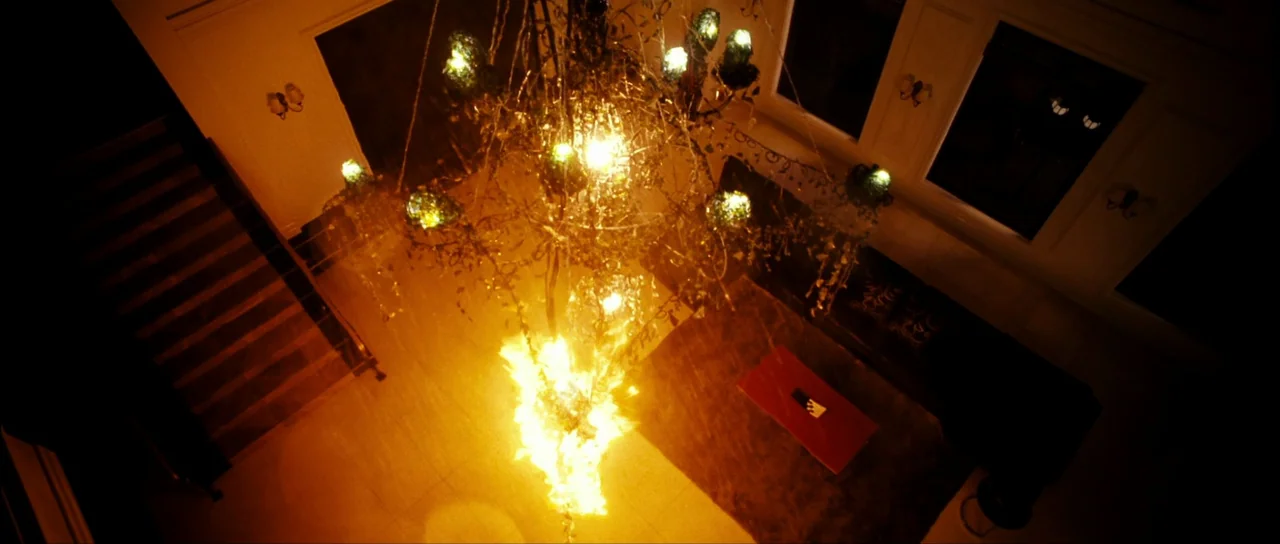 The Housemaid (2010) (2010) movie still: establishing — A high-angle view looks down upon a grand entryway with a burning chandelier. Fire blazes…