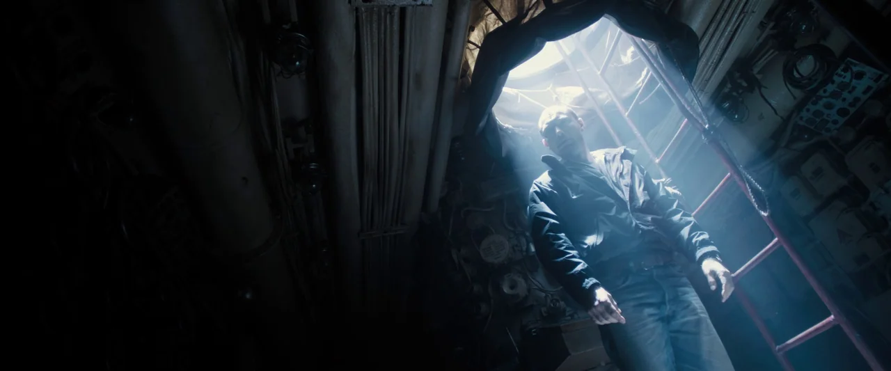Black Sea (2014) movie still: fullbody — A cramped, metallic enclosure with exposed pipes and technical dials on the walls. A man stands at the base…