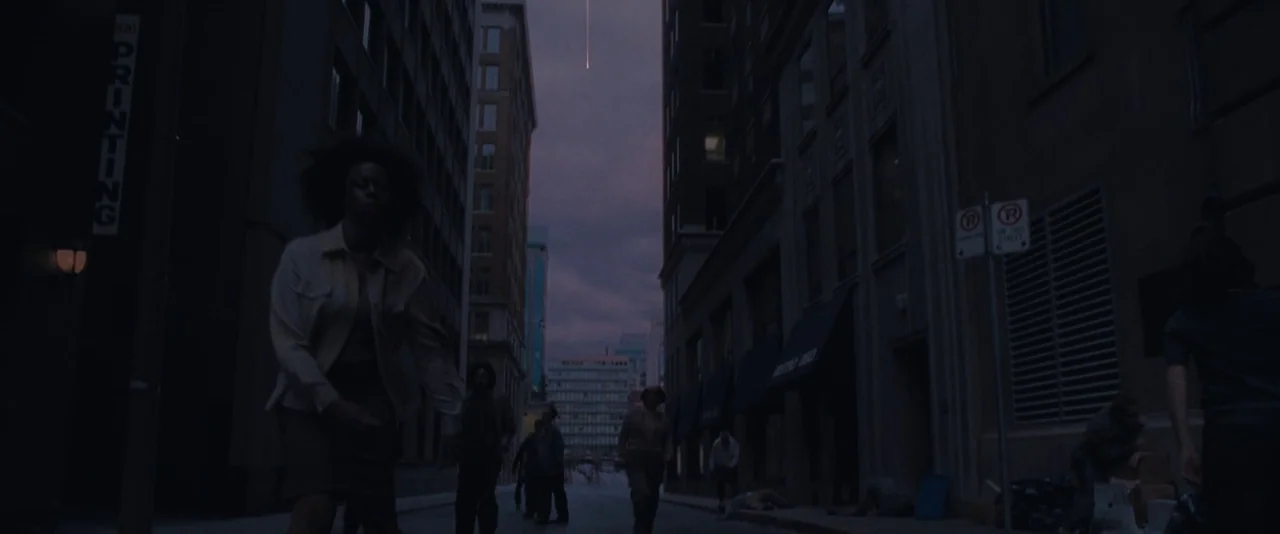 Resident Evil: Apocalypse (2004) movie still: wide — A desolate urban canyon features tall stone buildings flanking a narrow public road. A group of…